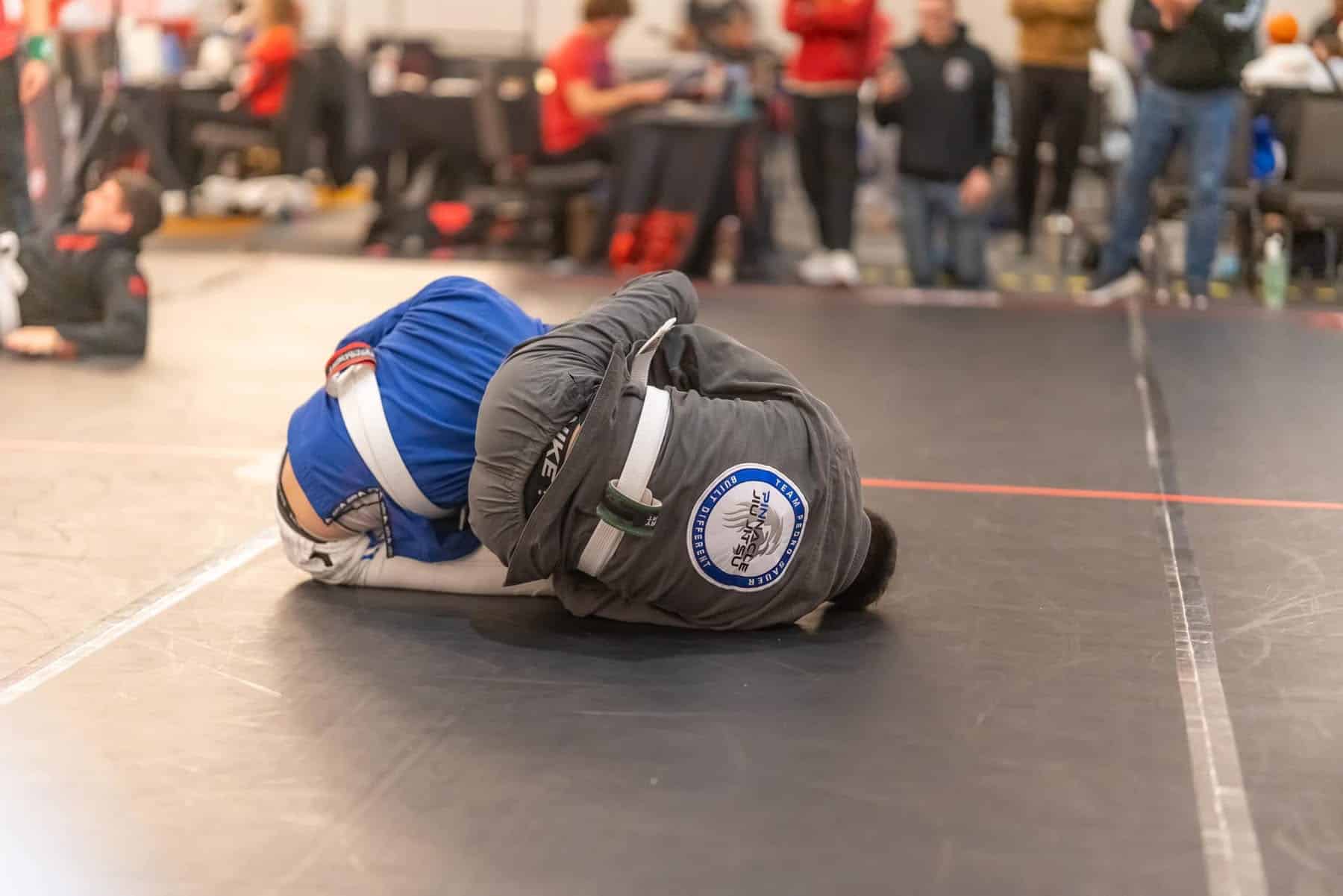 pinnacle jiu jitsu student in competition grappling on mat in gi