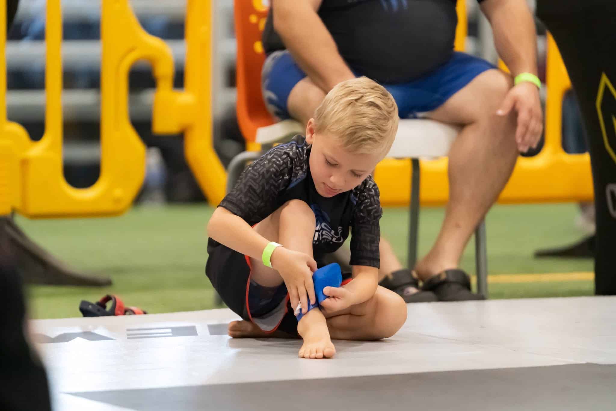 pinnacle jiu jitsu kid wrapping ankle on side of mat at competition event