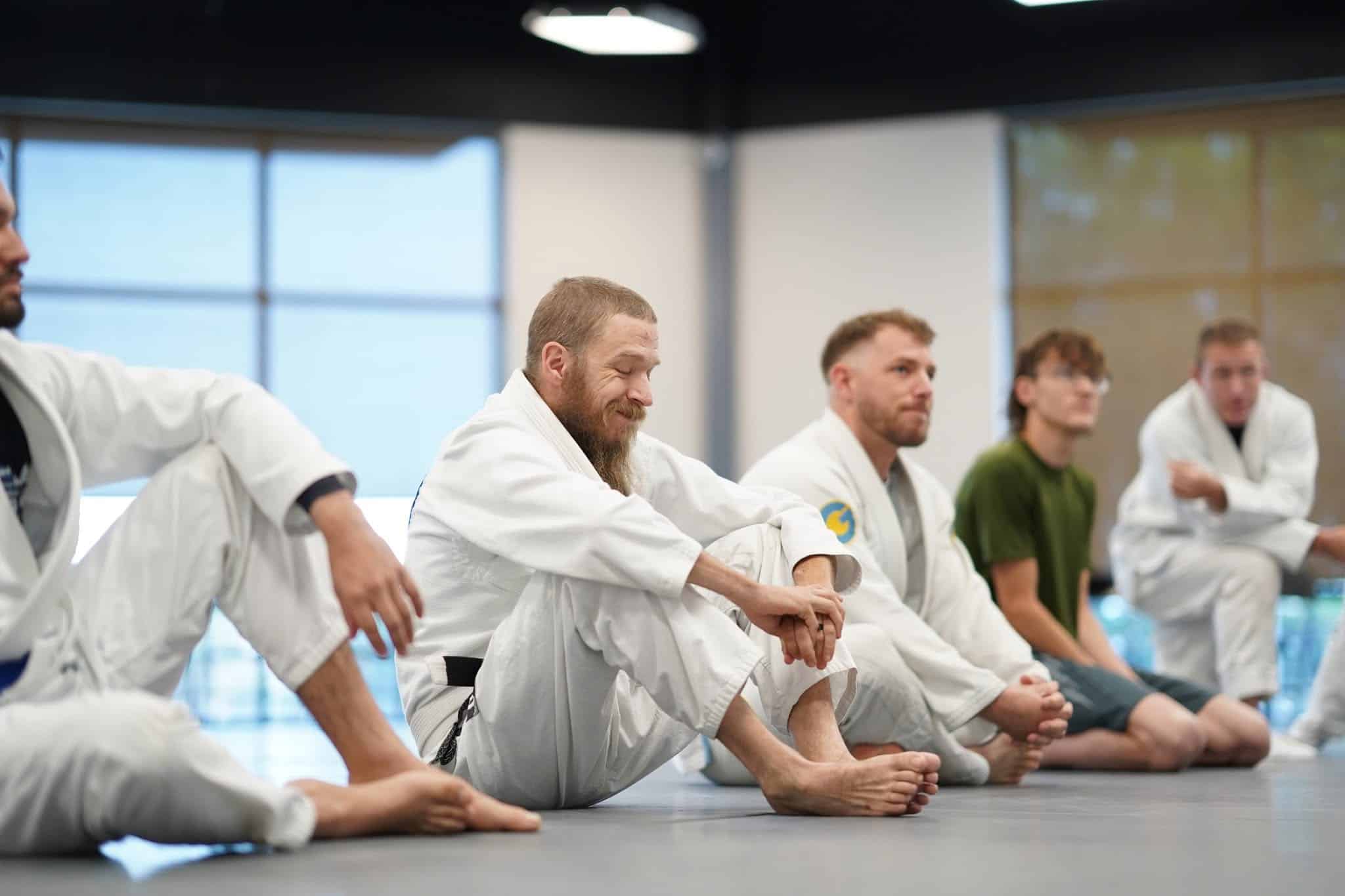Adult students at Pinnacle Jiu Jitsu sitting on mats wearing gi during lesson