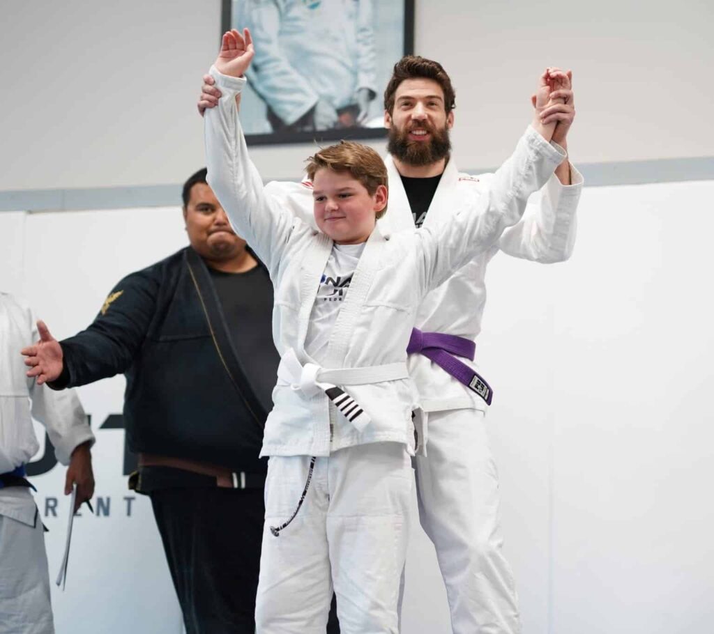 kids instructor holding up the hands of winning student for kids bjj class at Pinnacle Jiu Jitsu